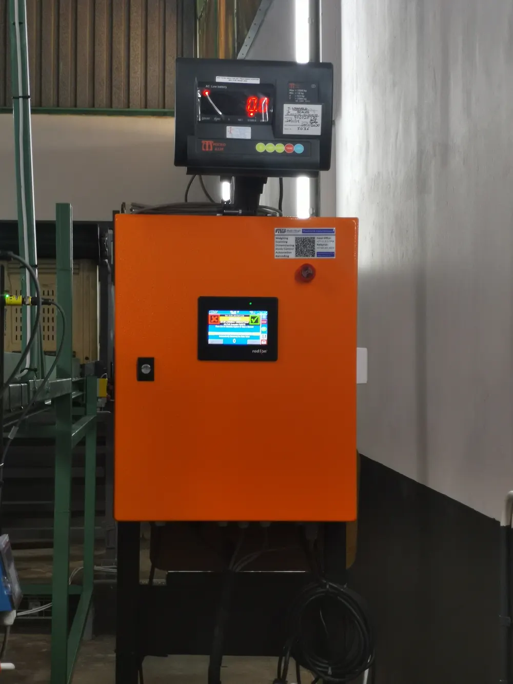 An orange control cabinet on a production line, with a touchscreen and a red LED weight indicator mounted on top
