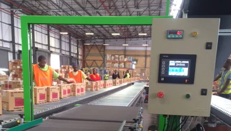 Workers packing cartons at a conveyor with an in-line checkweigher and control panel