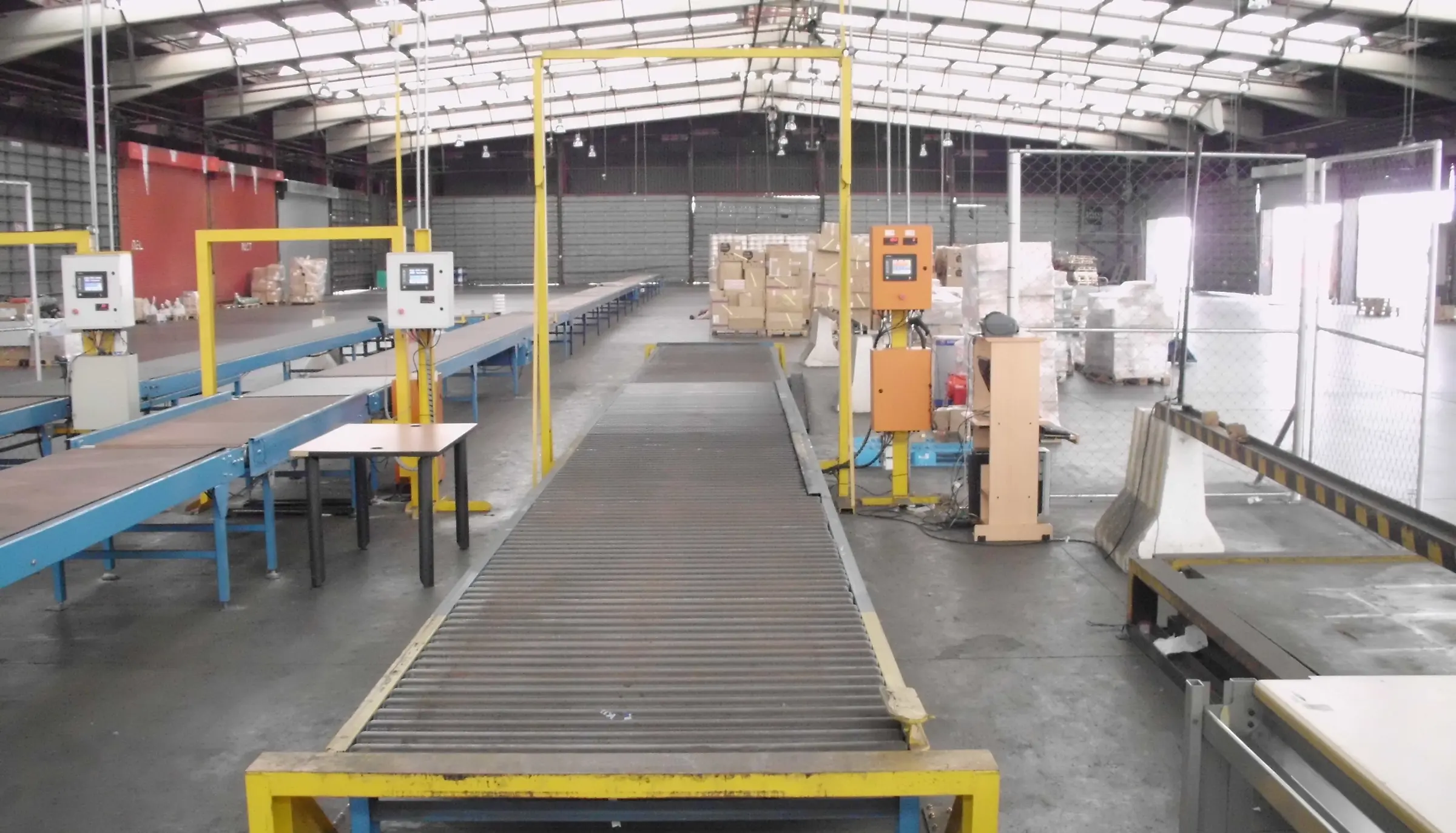 A long roller conveyor line in a warehouse with yellow dimensioning gantries and control panels