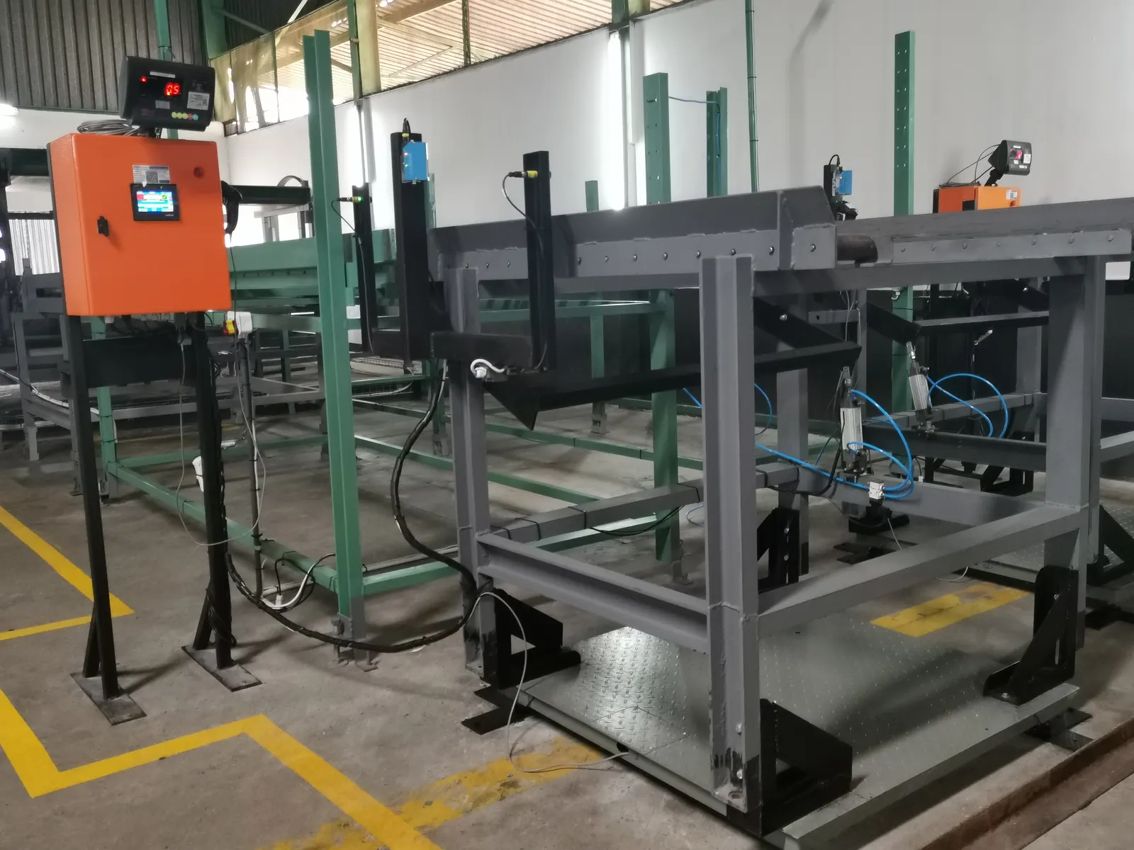 A weighing station on a production line: a grey steel frame with pneumatic arms, an orange control cabinet and a red LED weight indicator